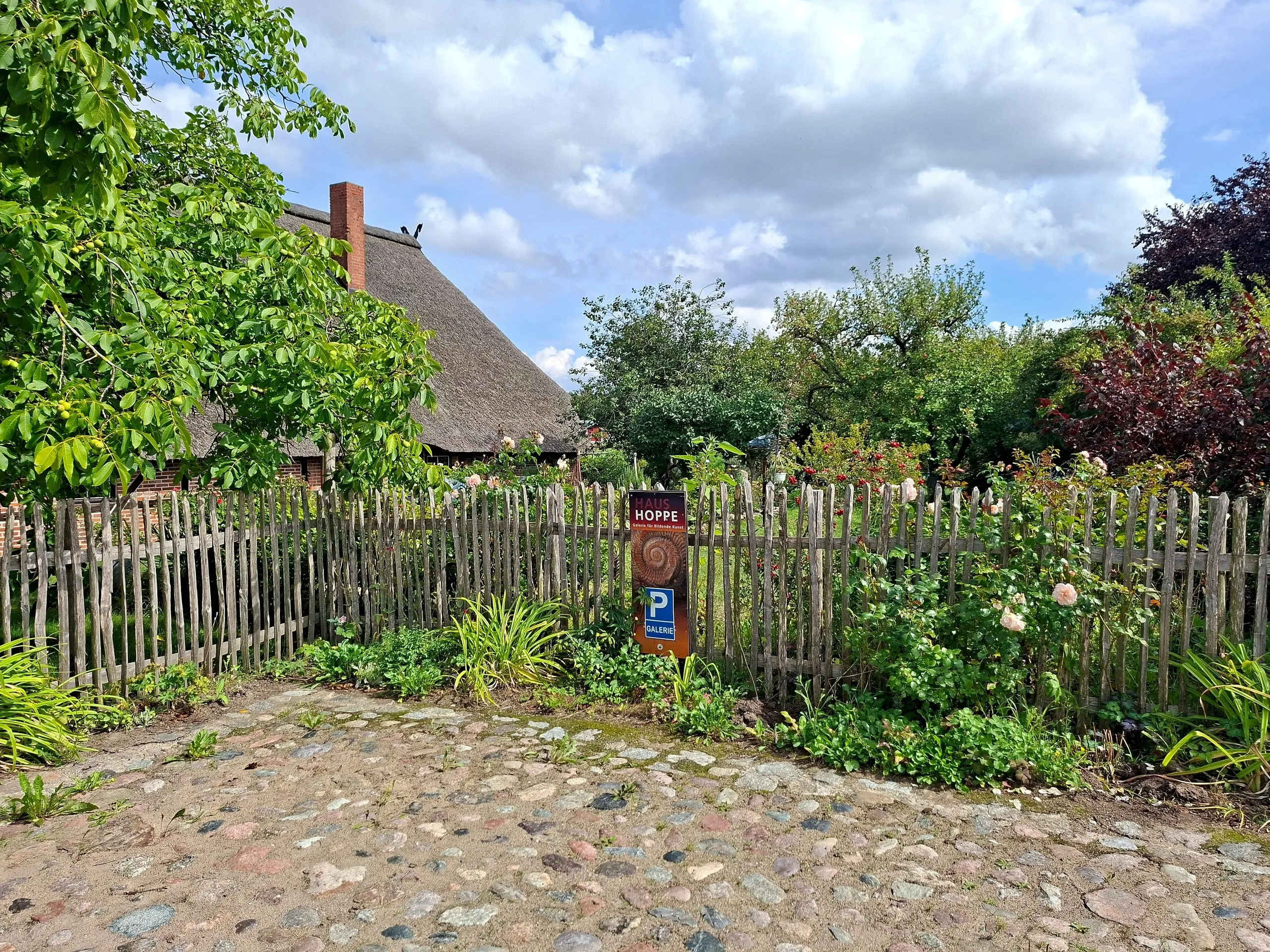 Cottage garden behind the picket fence, with a cobbled path and the HAUS HOPPE sign